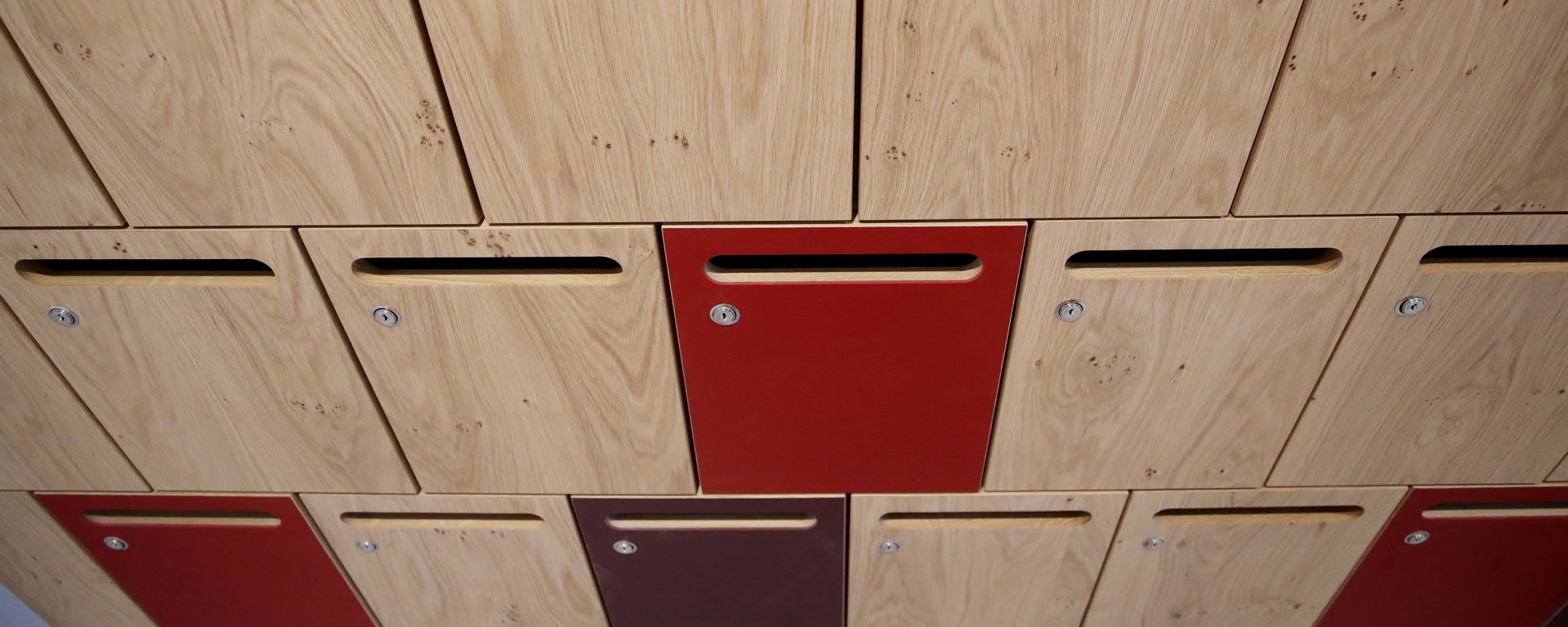 Detailansicht der Briefkastenwand mit naturholz farbenen und vereinzelt roten Briefklappen